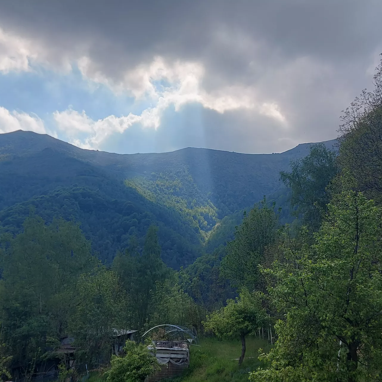 Sonnenstrahlen durchbrechen eine dichte Wolkendecke über einer hügeligen Landschaft Sonnenstrahlen durchbrechen eine dichte Wolkendecke über einer hügeligen Landschaft